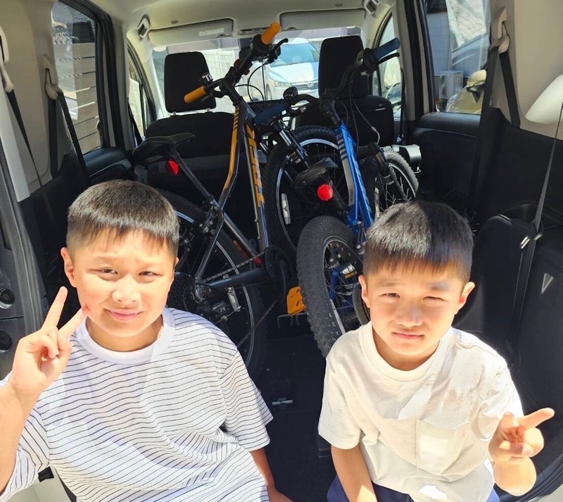 【写真】2人の男子小学生が自転車を積んだクルマの荷室に座っている