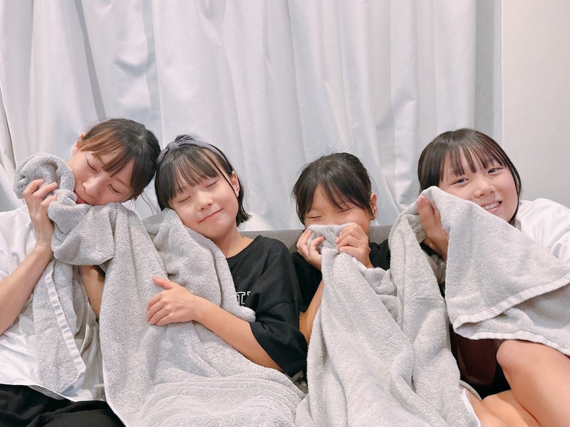 【写真】3人の女児とママが4人並んで座りグレーのバスタオルに頬ずりしている