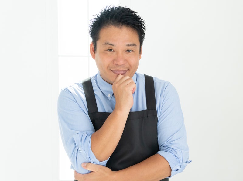 黒いエプロンを着てポーズを決めるレジェンド松下さんの写真