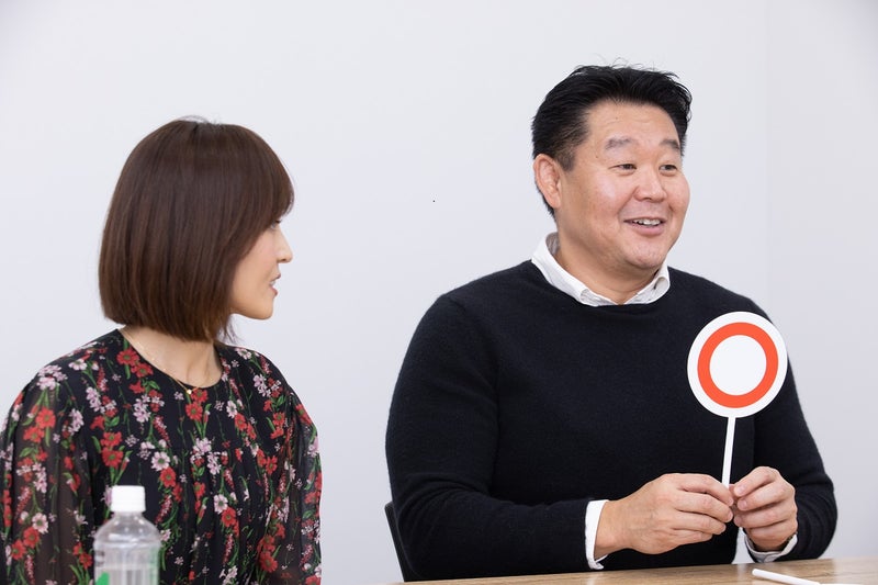 【写真】「〇」の札を出す花田虎上さんとみつめる倉実さん