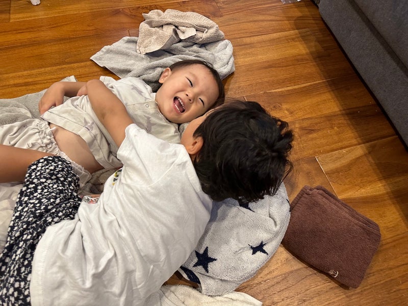 【写真】2人の小さな男児が洗濯物のうえでじゃれ合っている